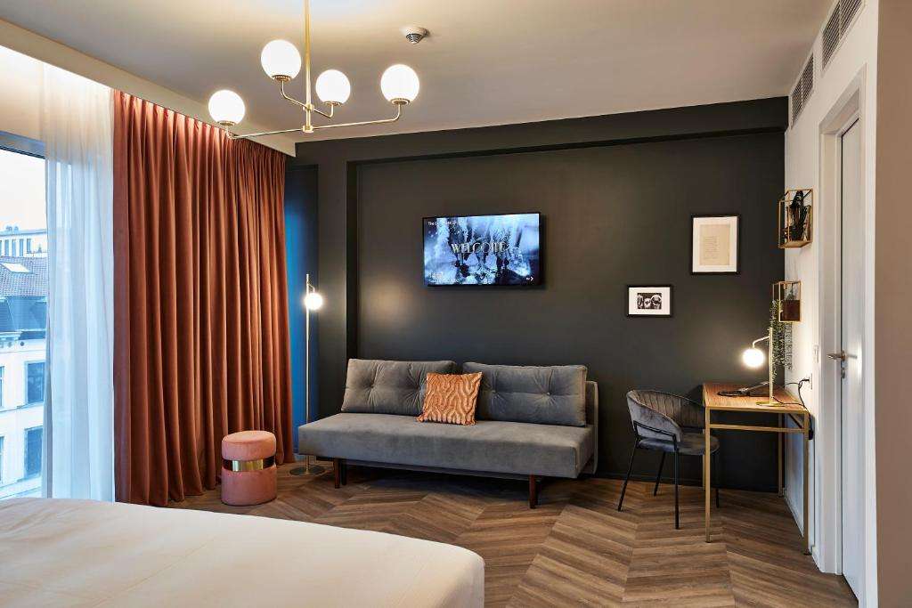 een slaapkamer met een bank en een tv aan de muur bij The Scott Hotel Brussels in Brussel